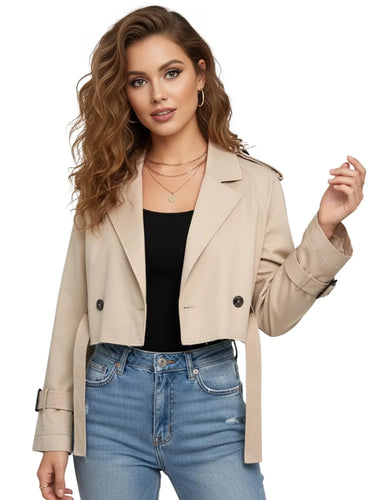Woman wearing a beige cropped trench coat, black top, and blue jeans on a white background